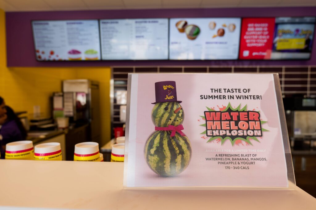 A refreshing Booster Juice Watermelon smoothie placed next to a Booster Juice hat, representing the brand's commitment to delicious and healthy beverages.