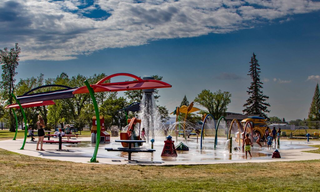 Children enjoying and playing at the Olds Splashpark, with water features in the background.