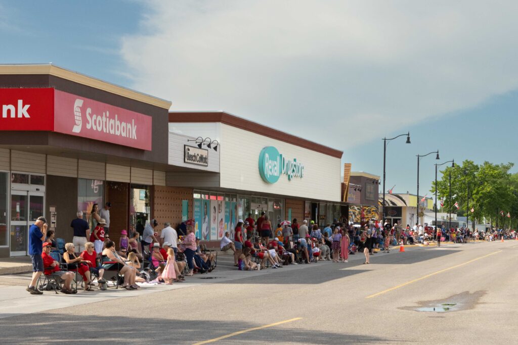 Crowds of locals and visitors line Main Street in Olds during a lively parade, with bustling shops and malls in the background, reflecting the town's strong community spirit and thriving retail sector.